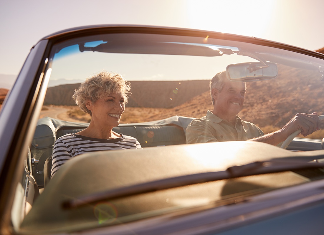 Auto Insurance - Closeup View of a Cheerful Elderly Couple Sitting in a Modern Convertible Car During a Road Trip Through the Desert