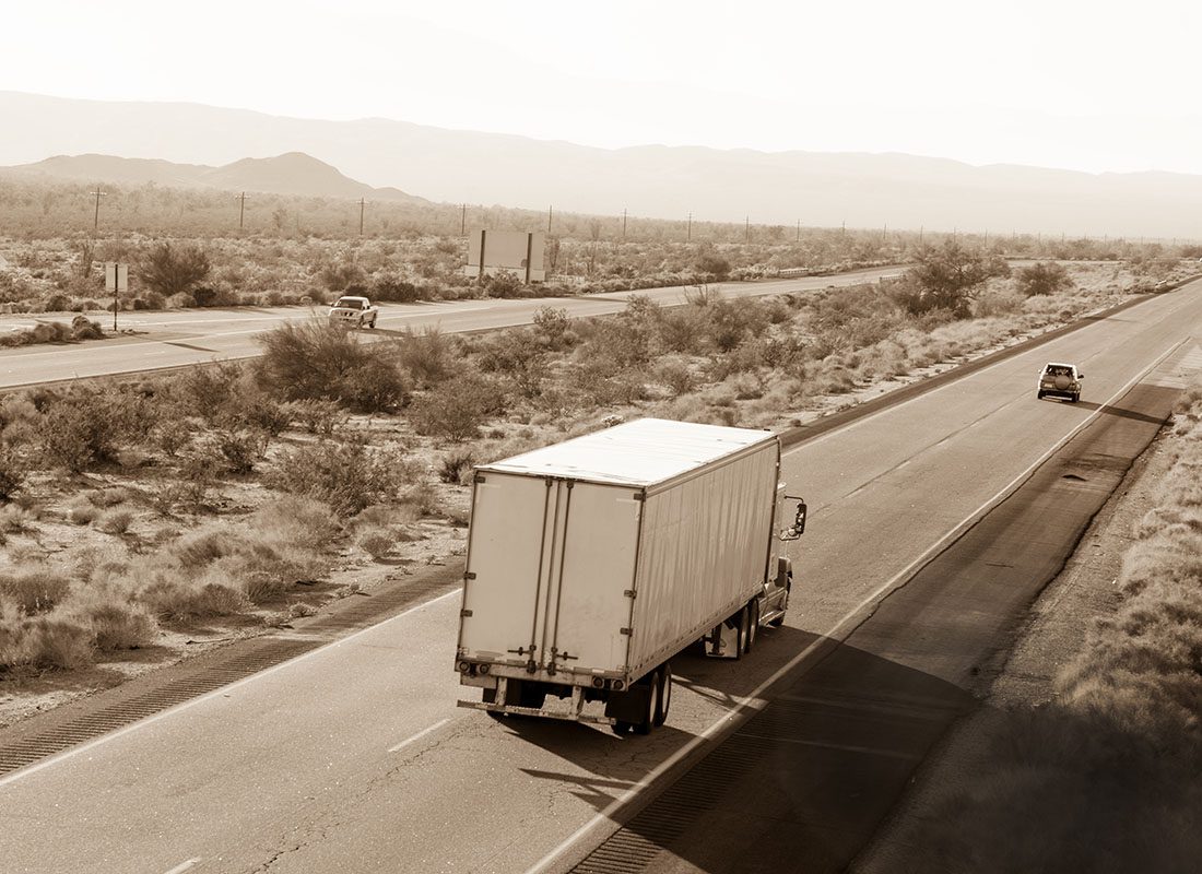 Trucking Insurance - View of a White Tractor Trailer Truck Driving Down a Highway Through the Desert