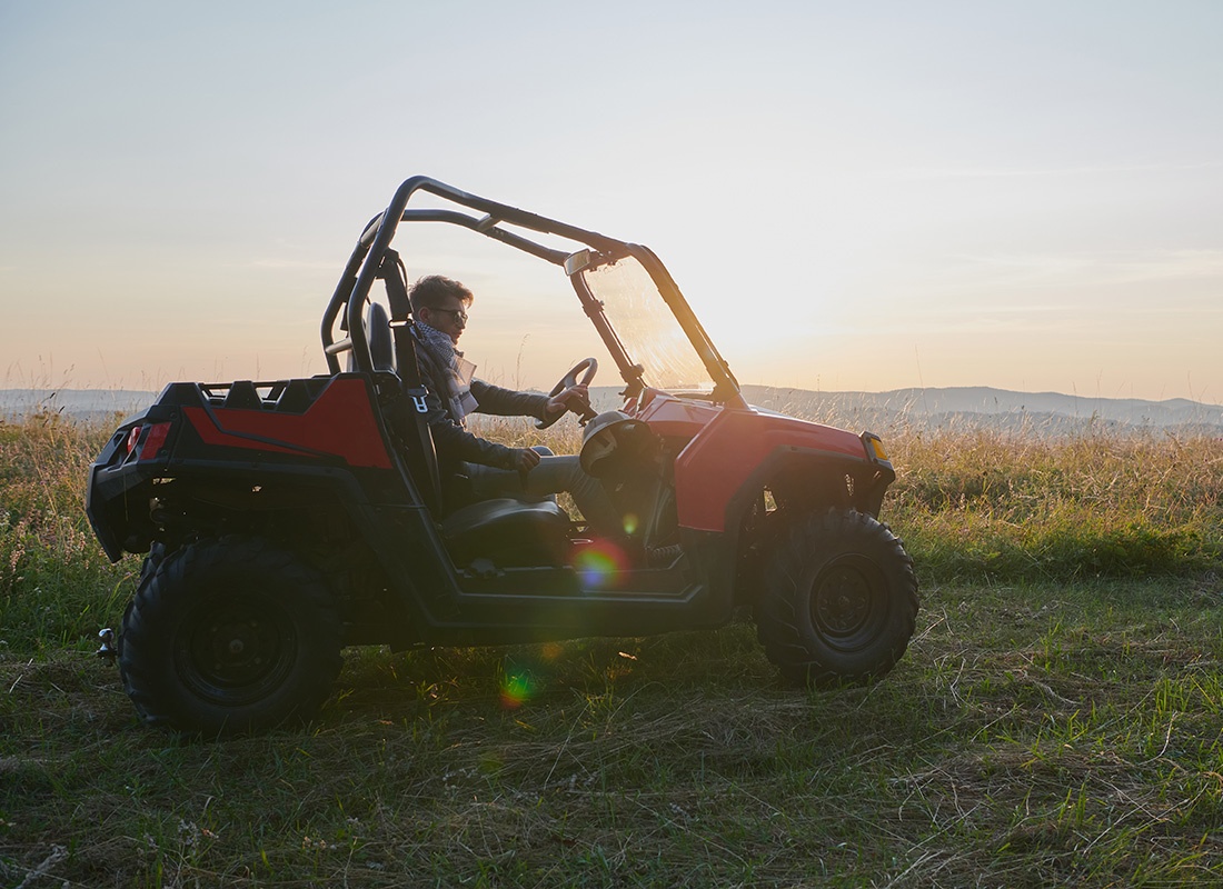 Off-Road Vehicle Insurance - View of a Man Riding a Red ATV on a Scenic Overlook with Views of the Mountains in the Distance at Sunset
